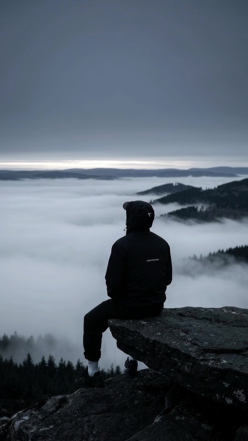 A man sitting on a rock above a sea of fog at dawn
